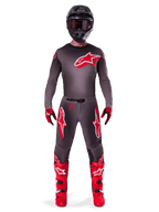 Motocross-Fahrer in kompletter Rennausrüstung, 2025 Supertech Lipan Jersey in Smoke Bright Red, passende graue Hose mit roten Logos, leuchtend rote Stiefel, schwarzer Helm mit Schutzbrille, rot-schwarze Handschuhe, professionelles Motocross-Outfit.