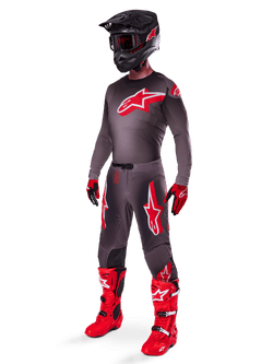 Ensemble d'équipement Alpinestars Supertech Lipan 2025, tenue de motocross complète, maillot gris foncé et rouge avec un grand logo en étoile, pantalon assorti avec des accents rouges et des graphismes d'étoiles, gants rouges et bottes rouge vif avec des boucles blanches, incluant un casque noir mat avec des lunettes rouges.