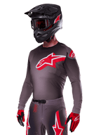 Ensemble d'équipement Alpinestars Supertech Lipan 2025, pilote de motocross portant un maillot et un pantalon gris foncé avec des accents rouges et blancs, doté d'un grand logo Alpinestars rouge sur la poitrine, perforations découpées au laser pour la ventilation, casque noir assorti, lunettes rouges et gants rouges et noirs