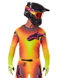 Motocross-Fahrer im 2025 Supertech Lipan Trikot, leuchtender Farbverlauf in Gelb, Orange und Pink, großes schwarzes Alpinestars Stern-Logo mit pinker Kontur auf der Brust, lasergeschnittene Perforationen zur Belüftung, athletische Rennpassform, kombiniert mit passender Hose, gelben Handschuhen und einem schwarzen Helm mit Brille.