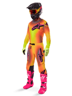 Motocross-Fahrer im Alpinestars Supertech Lipan Gear Set 2025, Trikot und Hose mit gelb-orangem Farbverlauf und pinken Akzenten, schwarzer Helm mit gelb-roter Brille, leuchtend gelbe Handschuhe und knallpinke Stiefel, abgestimmtes Offroad-Rennoutfit
