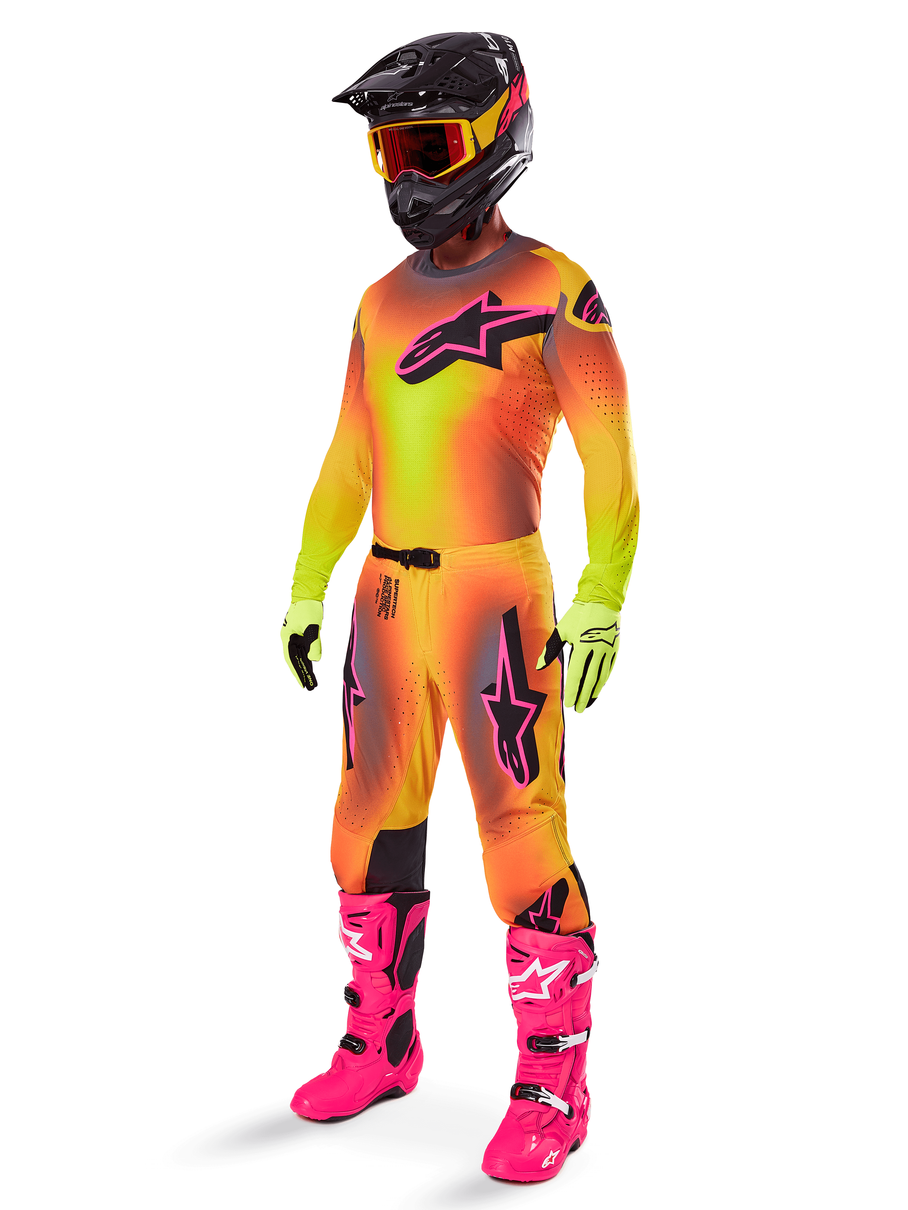 Motocross-Fahrer im Alpinestars Supertech Lipan Gear Set 2025, Trikot und Hose mit gelb-orangem Farbverlauf und pinken Akzenten, schwarzer Helm mit gelb-roter Brille, leuchtend gelbe Handschuhe und knallpinke Stiefel, abgestimmtes Offroad-Rennoutfit