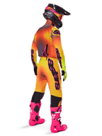 Motocross-Fahrer von hinten im Alpinestars 2025 Supertech Lipan Ausrüstungsset, gelb-orangefarbenes Trikot mit Farbverlauf und pinken Akzenten, passende Hose, leuchtend pinke Stiefel und schwarzer Helm mit pink-gelben Grafiken, koordiniertes Outfit für professionellen Rennsport