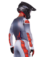 Pilote de motocross de dos portant le maillot Alpinestars Supertech Lipan 2025 en Gris Orange Fluo, avec des logos orange sur les manches et le dos, associé à un pantalon assorti et un casque noir, tenue de course professionnelle pour la performance tout-terrain.
