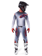 Pilote de motocross portant le maillot Alpinestars Supertech Lipan 2025 en Gris Orange Fluo, présentant un design dégradé gris et un logo orange, associé à un pantalon de motocross assorti, un casque noir, des bottes blanches et des gants orange, équipement de course coordonné de niveau professionnel.