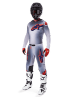 Pilote de motocross portant le maillot Alpinestars 2025 Supertech Lipan en gris et orange fluo, pantalon gris assorti avec des accents orange, casque noir, bottes blanches et noires, et gants orange et noirs, ensemble d'équipement professionnel pour la course tout-terrain