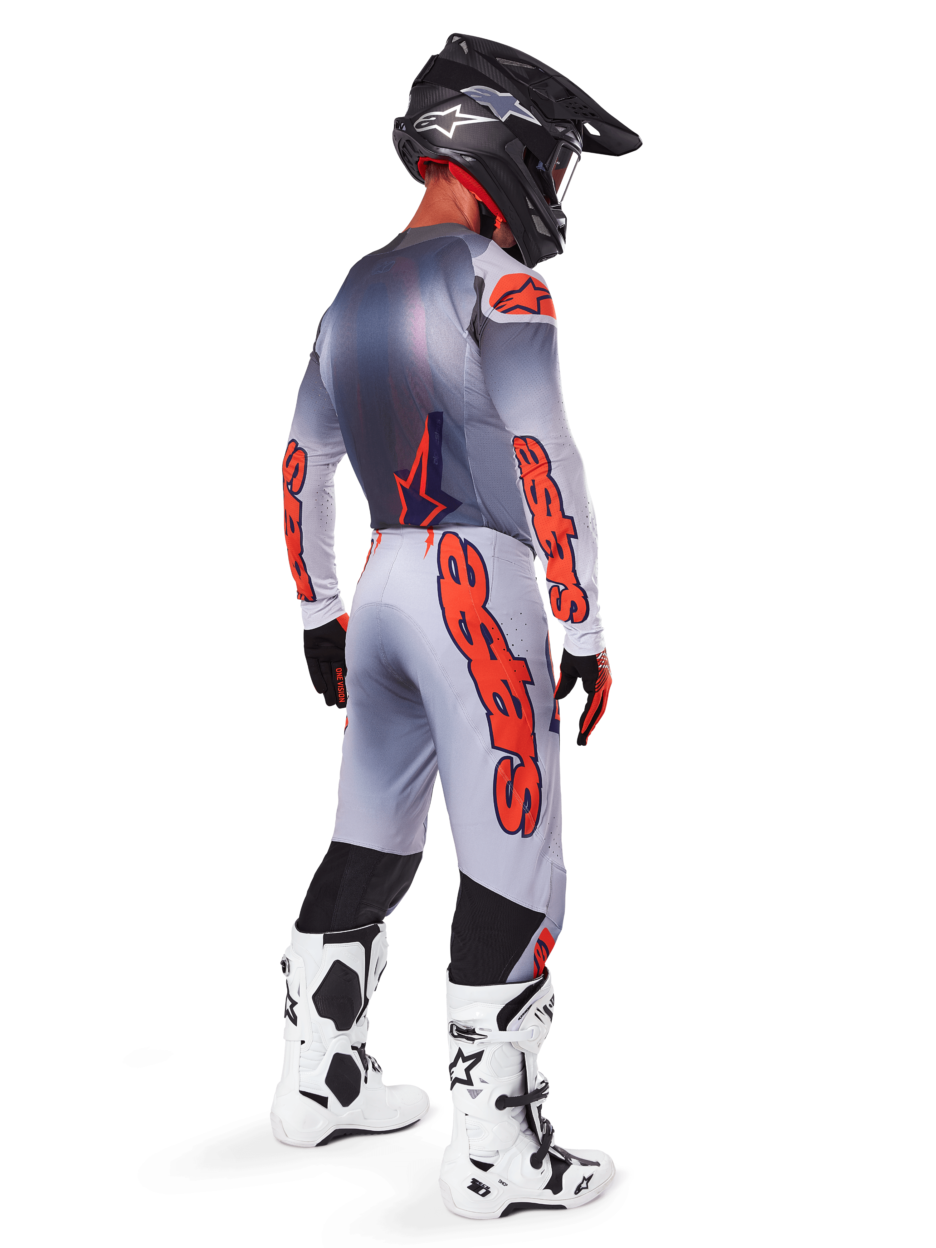 Pilote de motocross de profil arrière portant un maillot Supertech Lipan 2025 et un pantalon assorti en gris et orange fluo, avec le marquage Alpinestars orange vif sur les manches et les jambes, associé à un casque noir et des bottes blanches, tenue professionnelle coordonnée pour la course tout-terrain