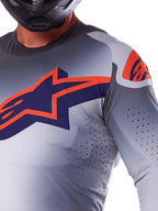 Gros plan d'un pilote portant le maillot Alpinestars 2025 Supertech Lipan, maillot de motocross, gris et orange fluo, avec un grand logo Alpinestars orange sur la poitrine, des perforations de ventilation découpées au laser et un casque noir, équipement de course professionnel.