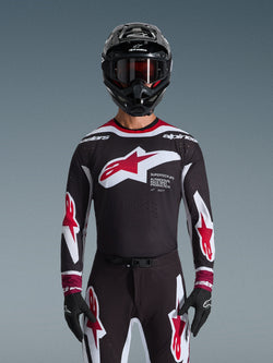 Alpinestars 2026 Supertech AFD Vista Jersey, motorcross shirt in zwart, rood en wit, getoond op een rijder met een zwarte helm, crossbril en handschoenen, voorzien van een groot logo op de borst en 'SUPERTECH AFD' branding, professionele racekleding voor off-road prestaties