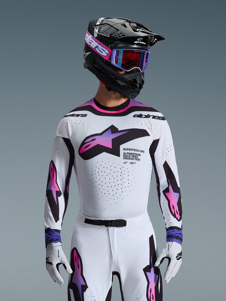 Motocross rider wearing the 2026 Supertech AFD Vista Jersey in White Purple and Black, featuring a black helmet with pink branding, purple goggles, and matching white gloves, athletic fit gear designed for professional off-road racing performance