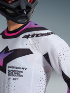 Close-up of a motocross rider wearing the 2026 Supertech AFD Vista Jersey in White Purple Black, featuring laser-cut perforations for ventilation, "SUPERTECH AFD" text on the chest, and black Alpinestars branding on the shoulder, athletic-fit off-road racing apparel.