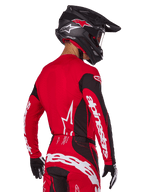 Motocross-Fahrer in der Rückansicht im Alpinestars 2025 Techstar Dreem Gear Set, rot-schwarzes Jersey mit weißem Branding an den Ärmeln, passende rot-schwarze Hose mit markantem weißem Logo auf dem Gesäß, schwarzer Carbon-Helm mit roten Akzenten, schwarz-weiße Handschuhe, professionelles Offroad-Rennoutfit.