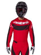 Alpinestars 2025 Techstar Dreem Trikot, Motocross-Ausrüstung, Hellrot und Schwarz, mit weißem „astars“-Logo und schwarzem, belüftetem Brustpanel, getragen mit passender Hose, schwarzem Helm und weiß-schwarzen Handschuhen, konzipiert für professionellen Offroad-Rennsport