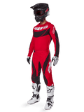 Ganzkörperansicht eines Motocross-Fahrers im 2025 Techstar Dreem Gear Set in Hellrot und Schwarz, mit einem Performance-Trikot mit weißem Branding, passender Stretch-Ripstop-Hose, einem schwarzen Helm mit rotem Visier, weiß-schwarzen Handschuhen und weißen Tech-Stiefeln, spezialisierte Rennausrüstung für Offroad-Wettbewerbe.