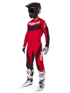 Ganzkörperansicht eines Motocross-Fahrers im 2025 Techstar Dreem Gear Set in Hellrot und Schwarz, mit einem Performance-Trikot mit weißem Branding, passender Stretch-Ripstop-Hose, einem schwarzen Helm mit rotem Visier, weiß-schwarzen Handschuhen und weißen Tech-Stiefeln, spezialisierte Rennausrüstung für Offroad-Wettbewerbe.
