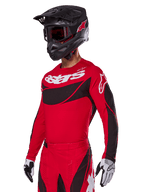 Alpinestars 2025 Techstar Dreem Gear Set, rotes Motocross-Trikot und Hose mit schwarzen und weißen Akzenten, getragen mit schwarzem Helm und Goggles, weiße und schwarze Handschuhe, markantes „astars“-Branding, konzipiert für Performance-Offroad-Rennsport