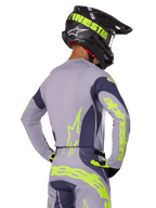 Motocross-Fahrer in der Rückansicht im Alpinestars 2025 Techstar Dreem Gear Set, graues Jersey und Hose mit leuchtend neongelbem Branding, passender schwarzer Helm mit Neon-Grafiken, professionelle Motocross-Rennausrüstung