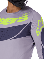 Alpinestars 2025 Techstar Dreem Jersey, Motocross-Jersey, Grau und Navy-Blau mit leuchtend lindgrünem Logo, Nahaufnahme eines Fahrers mit schwarzem Helm, mit lasergeschnittenen Perforationen zur Belüftung