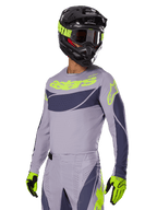 Motocross-Fahrer im Alpinestars 2025 Techstar Dreem Trikot in Grau und Dunkelgrau, mit neongelbem „astars“-Logo auf der Brust, kombiniert mit passendem Helm, Schutzbrille und Handschuhen für einen koordinierten Offroad-Rennsport-Look