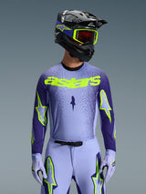 Alpinestars 2026 Supertech Scenz Jersey, motorcross jersey, paars en fluorgeel, gedragen door een rijder met een bijpassende zwart-paarse helm, neongele crossbril en paarse crossbroek, voorzien van neongeel astars-logo op de borst en sterlogo's op de mouwen.