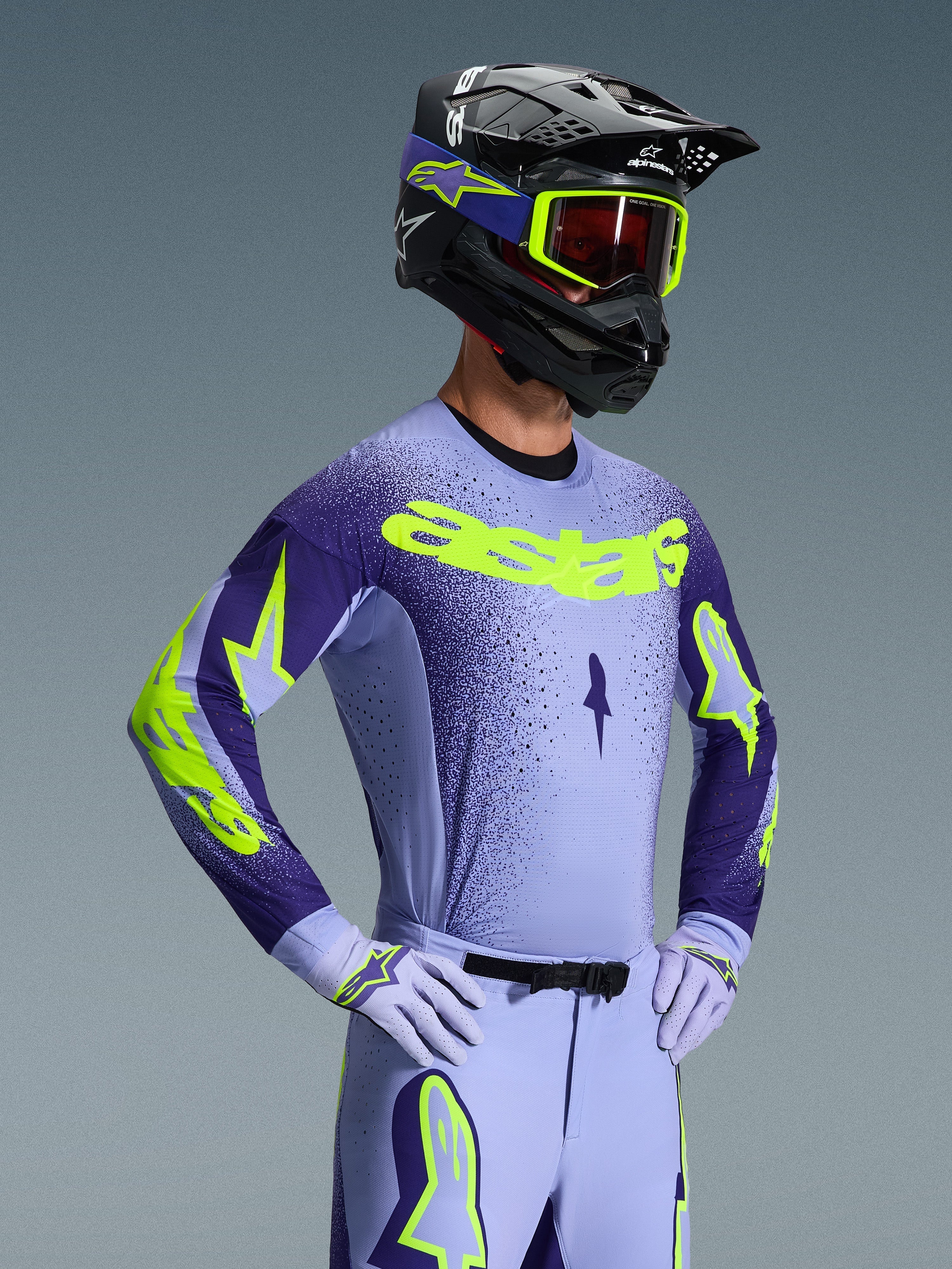 Alpinestars 2026 Supertech Scenz Ausrüstungsset, Motocross-Fahrer in lavendel- und dunkelvioletter Rennausrüstung mit neongelben Akzenten, passender Helm und Goggles, sportliches Pro-Fit Jersey und Hose mit markantem Branding