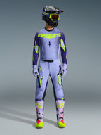 Motocross-Fahrer in kompletter Alpinestars 2026 Supertech Scenz Rennausrüstung, Trikot in Lila und Gelb Fluo mit passender Hose, schwarzer Helm mit gelber Schutzbrille, helllila und neonfarbene Stiefel, professionelles Outfit mit athletischer Passform für den Offroad-Rennsport