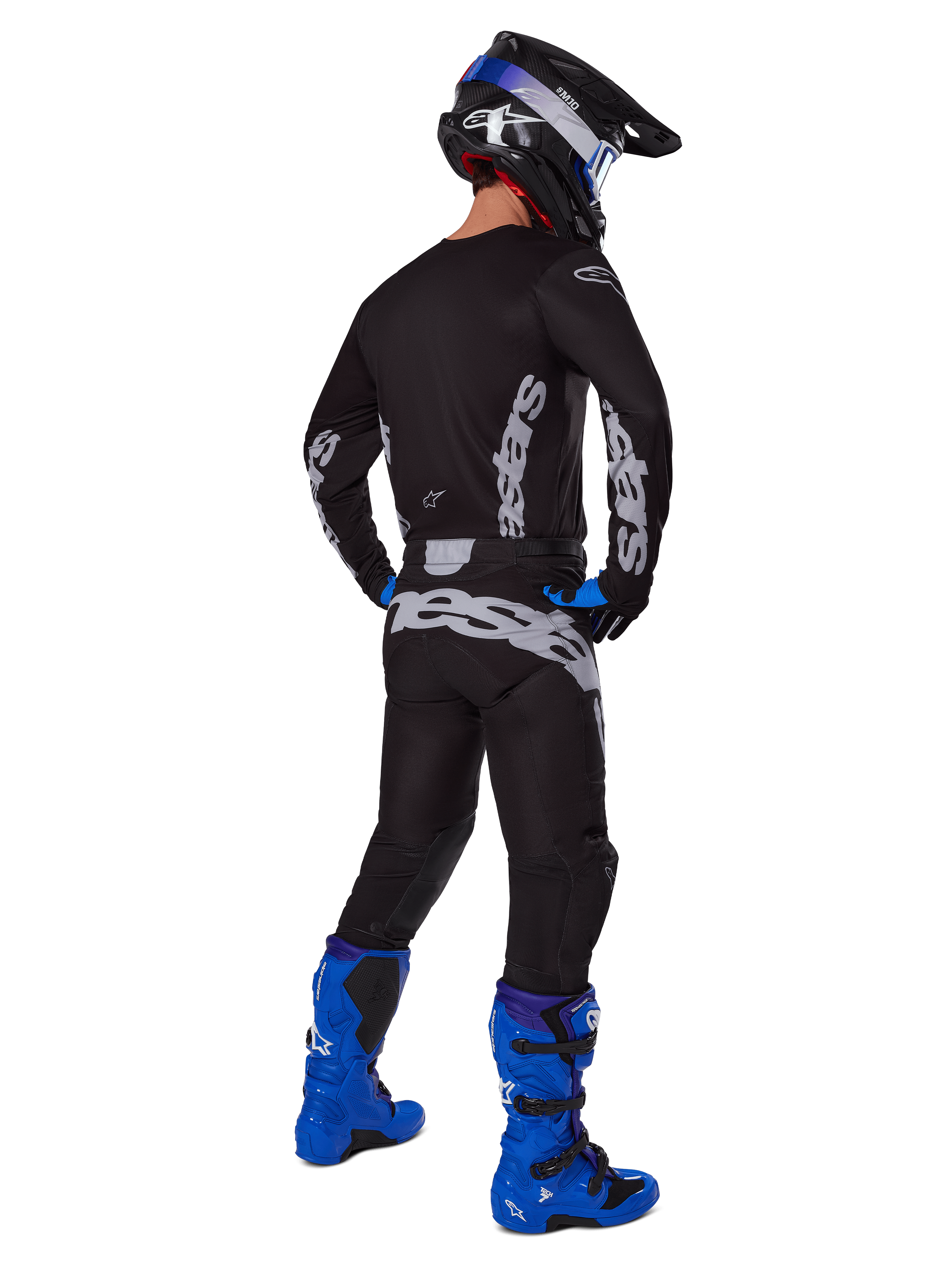 Pilote de motocross vu de dos portant l'ensemble d'équipement Alpinestars 2025 Racer Graphite, maillot et pantalon noir et gris avec logos gris, assortis à des bottes de motocross bleu vif, un casque noir et bleu et des gants bleus, tenue tout-terrain de performance complète.