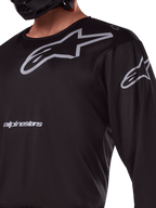 Maillot Alpinestars 2025 Racer Graphite, noir et gris, gros plan d'un pilote portant un maillot de motocross, avec marquage Alpinestars gris et logos A-star, matériau technique en poly-tissu pour la conduite tout-terrain