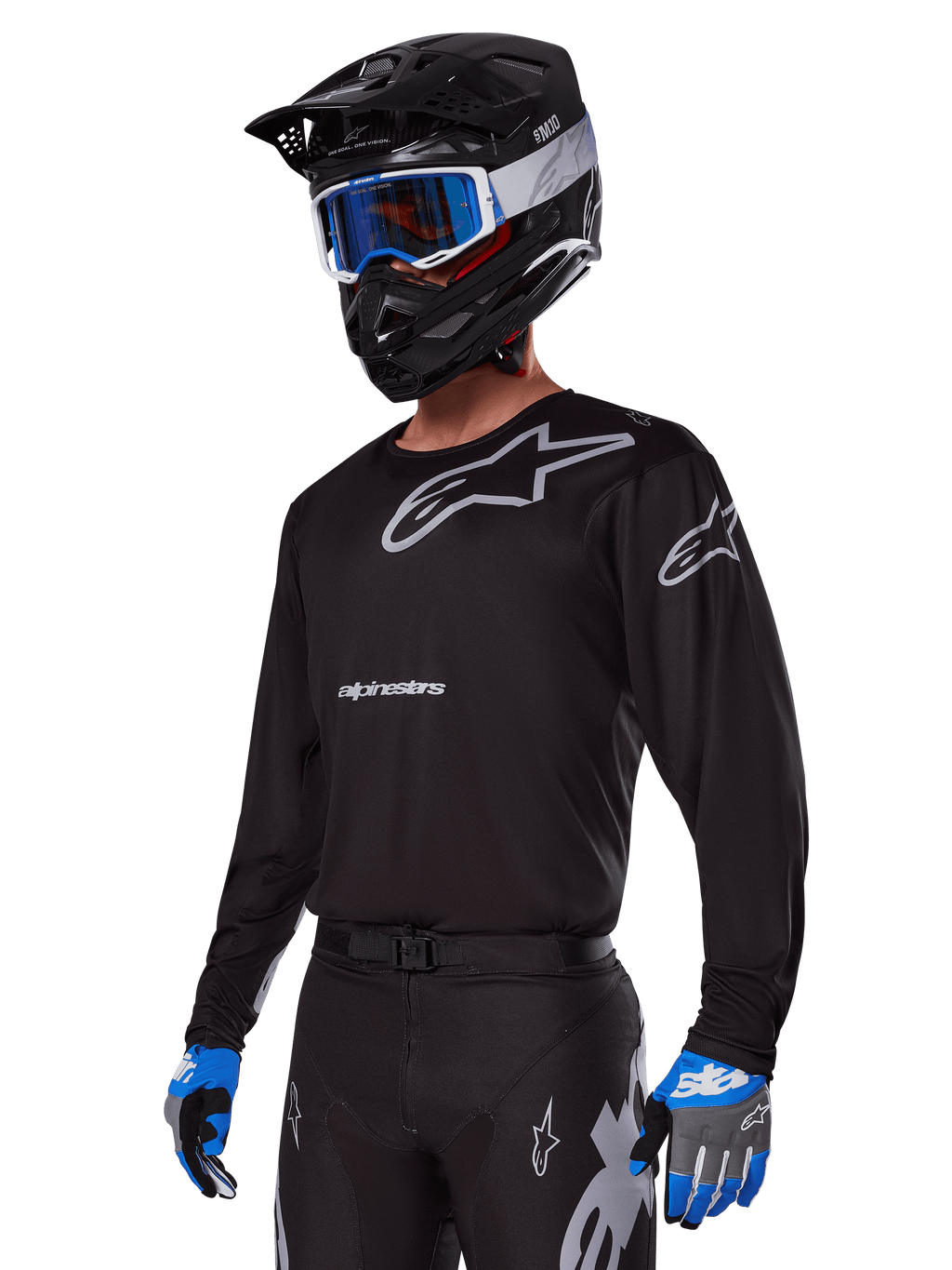 Motocross rider wearing Alpinestars 2025 Racer Graphite Gear Set, Black jersey with grey Alpinestars logos, matching black pants with grey accents, black helmet with blue and white goggles, blue and grey gloves, sleek technical outfit for off-road racing
