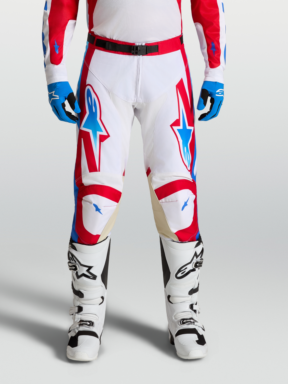 Alpinestars Pantalons Racer Hunt, pantalons de motocross homme, blancs, rouges et bleus, jambes pré-courbées ergonomiques, panneaux de genoux en cuir, portés avec bottes et gants assortis