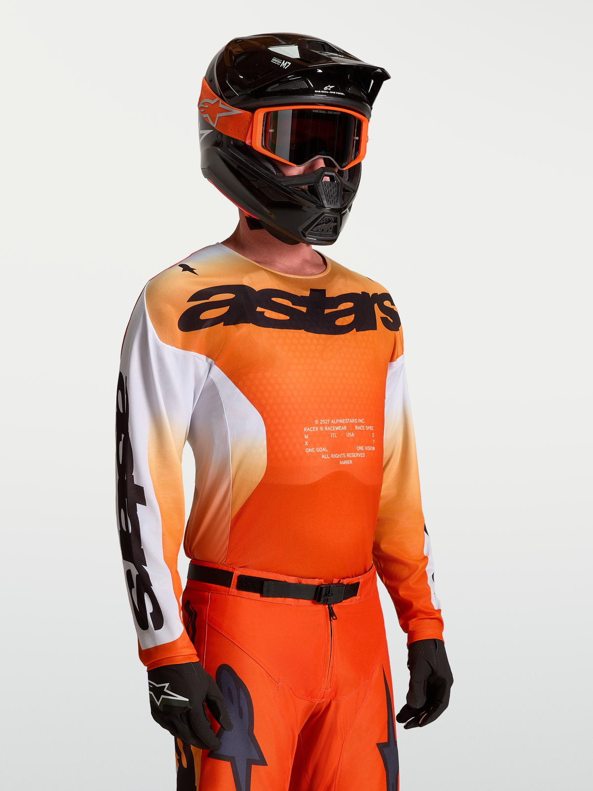 Maillot Alpinestars Racer Amber, maillot de motocross pour homme, orange et blanc, porté avec casque et gants, coupe racing