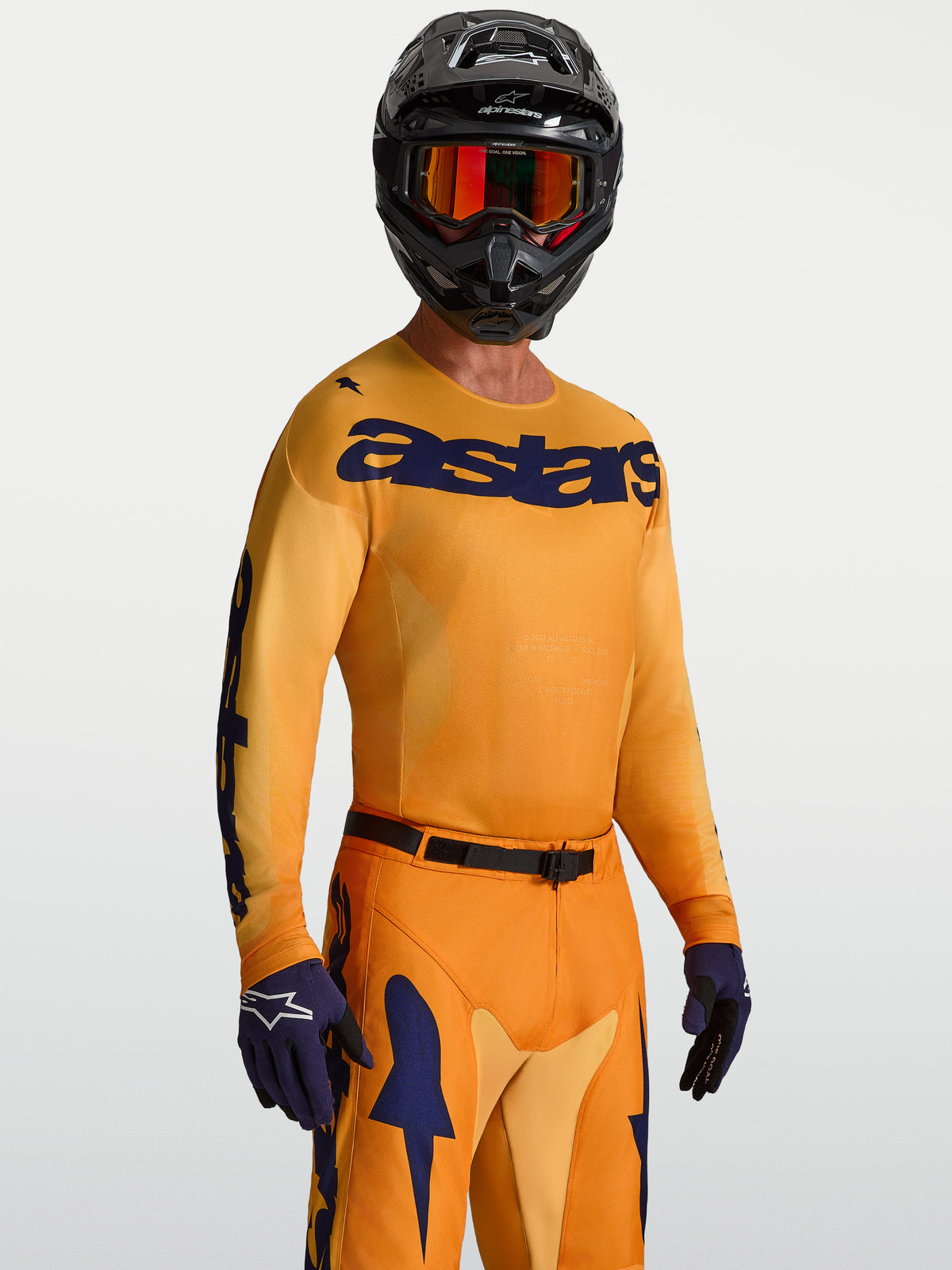 Maillot Alpinestars Racer Amber, maillot de motocross pour homme, orange et bleu foncé, en poly-tissu léger évacuant l'humidité, porté par un mannequin avec un casque intégral.