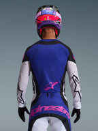 Rückansicht eines Motocross-Fahrers im 2026 Techstar Knif Jersey in Black Light Gray Purple, mit einer lila Rückenpartie und einem pinkfarbenen Alpinestars-Logo, hellgrauen Ärmeln mit schwarzen Akzenten und lasergeschnittenen Perforationen, kombiniert mit einem passenden pink-lila Helm und schwarzen Handschuhen.