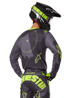Motorcrossrijder van achteren gezien in de 2025 Racer Hollow Gear Set, grijze jersey met fluorescerend gele cirkelvormige tekst en sterlogo's, bijpassende grijze en gele broek met opvallende branding op het zitvlak, zwarte en limoengroene helm, gecoördineerde outfit voor off-road racen