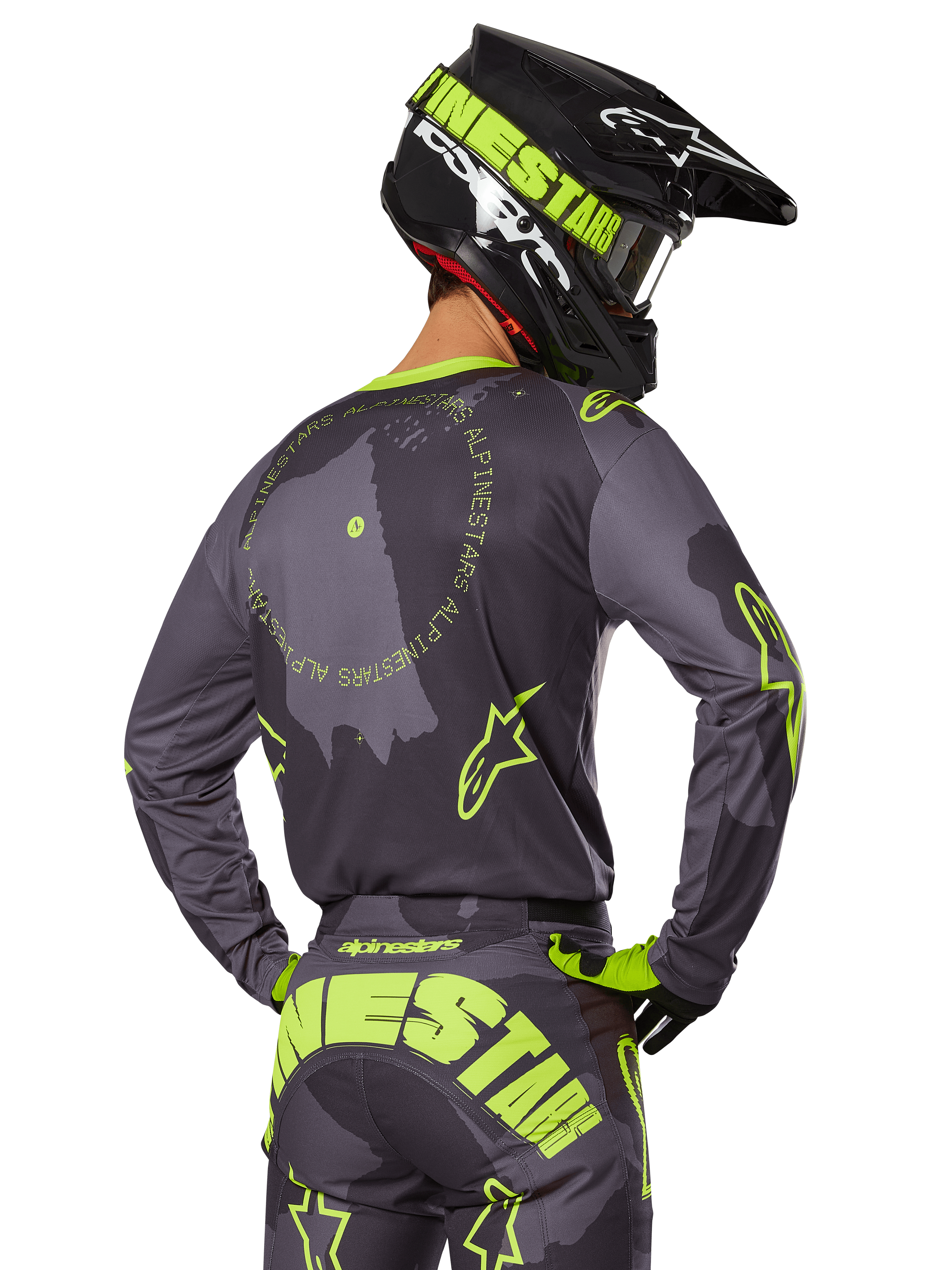 Motorcrossrijder van achteren gezien in de 2025 Racer Hollow Gear Set, grijze jersey met fluorescerend gele cirkelvormige tekst en sterlogo's, bijpassende grijze en gele broek met opvallende branding op het zitvlak, zwarte en limoengroene helm, gecoördineerde outfit voor off-road racen