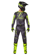 Pilote de motocross portant un équipement de course complet, maillot Alpinestars Racer Hollow 2025 et pantalon assorti en Dark Camo Yellow Fluo, avec des graphismes jaune fluo éclatants sur un fond camouflage gris foncé, gants assortis, bottes jaune fluo et casque noir.