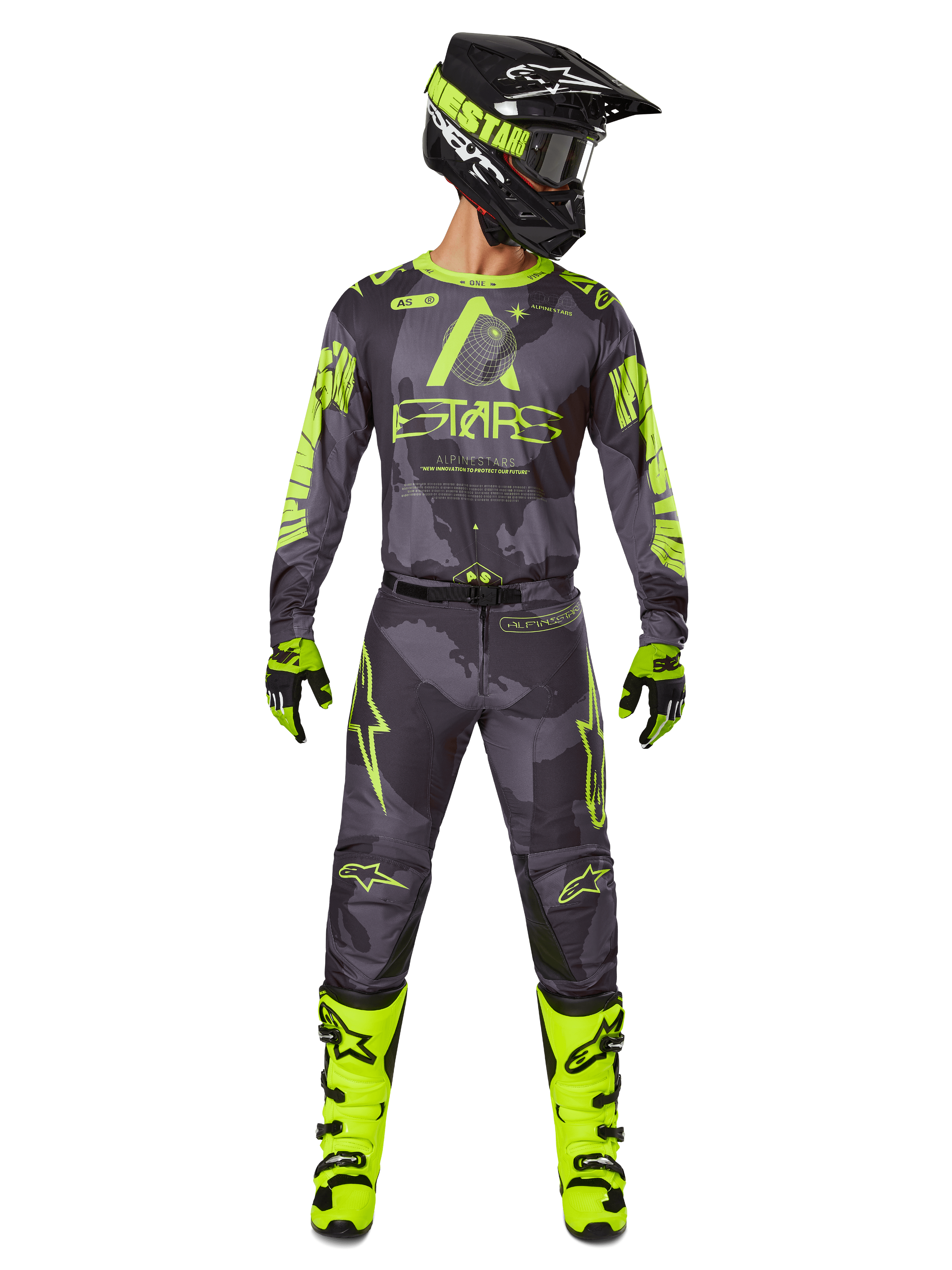 Pilote de motocross portant un équipement de course complet, maillot Alpinestars Racer Hollow 2025 et pantalon assorti en Dark Camo Yellow Fluo, avec des graphismes jaune fluo éclatants sur un fond camouflage gris foncé, gants assortis, bottes jaune fluo et casque noir.
