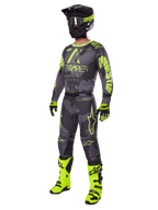 Pilote de motocross portant l'ensemble d'équipement Alpinestars Racer Hollow 2025, maillot et pantalon Dark Camo et jaune fluo, casque noir et jaune fluo, gants assortis et bottes jaune fluo éclatant, tenue coordonnée pour la course tout-terrain