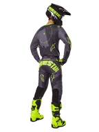 Achteraanzicht van een motorcrosser die de 2025 Racer Hollow Gear Set draagt in Dark Camo Yellow Fluo, voorzien van een grijs camo jersey met geel fluo accenten, bijpassende motorcrossbroek met opvallende branding op het zitvlak, felgele fluo laarzen en een zwarte helm met gele bril.