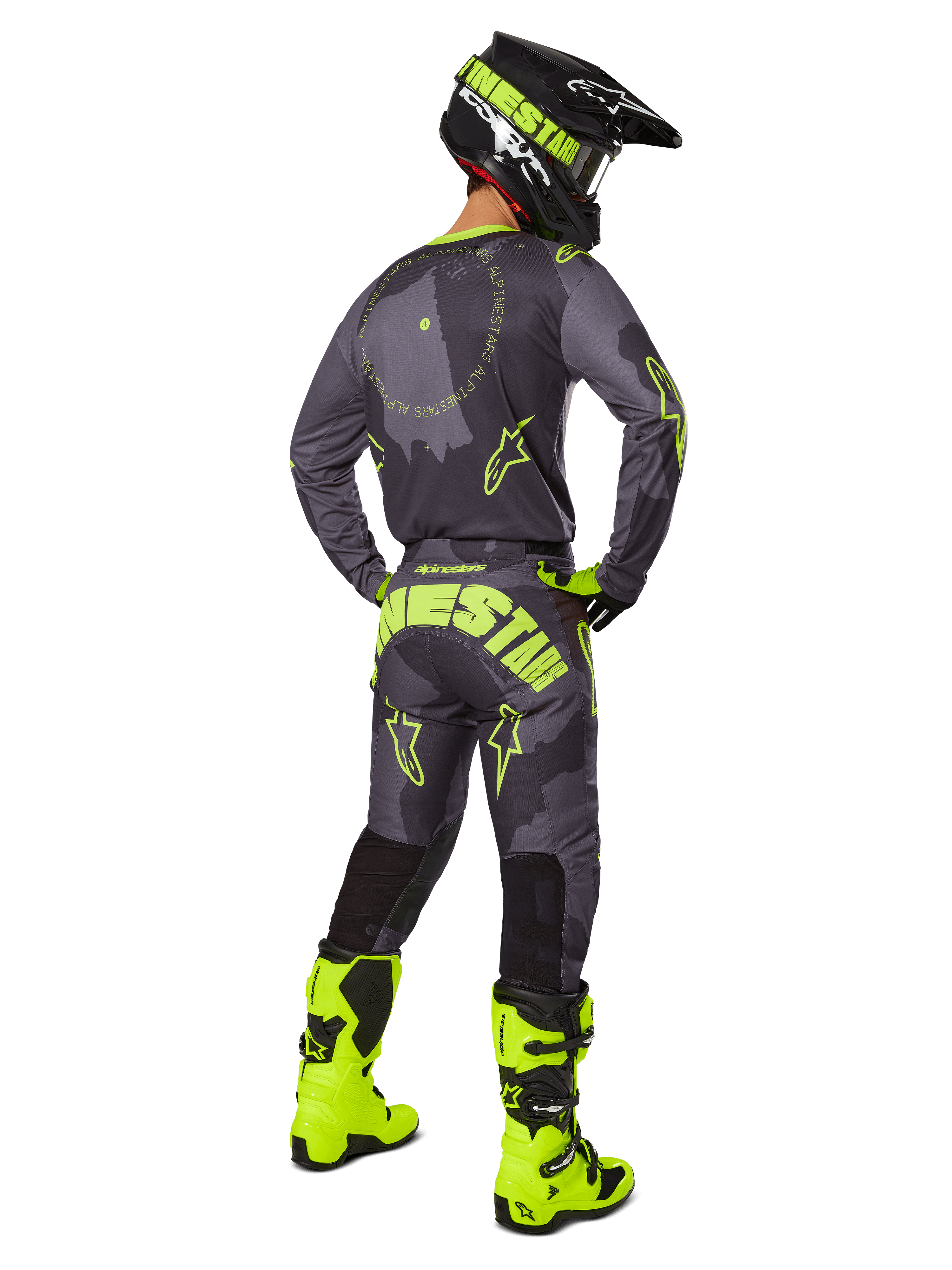 Achteraanzicht van een motorcrosser die de 2025 Racer Hollow Gear Set draagt in Dark Camo Yellow Fluo, voorzien van een grijs camo jersey met geel fluo accenten, bijpassende motorcrossbroek met opvallende branding op het zitvlak, felgele fluo laarzen en een zwarte helm met gele bril.