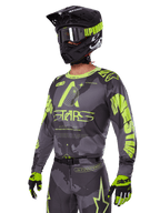 Alpinestars 2025 Racer Hollow Gear Set, motorcross jersey en broek in grijs en neongeel, gedragen met bijpassende zwarte helm, crossbril en handschoenen, opvallende fluorescerende gele Alpinestars-branding en ster-graphics op een grijze basis met patroon, professionele off-road racing look