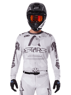 Alpinestars 2025 Racer Hollow Jersey, Motocross Jersey, White and Black, worn with matching white MX pants and a black helmet with orange goggles, featuring bold Alpinestars branding and globe graphics, professional off-road racing gear