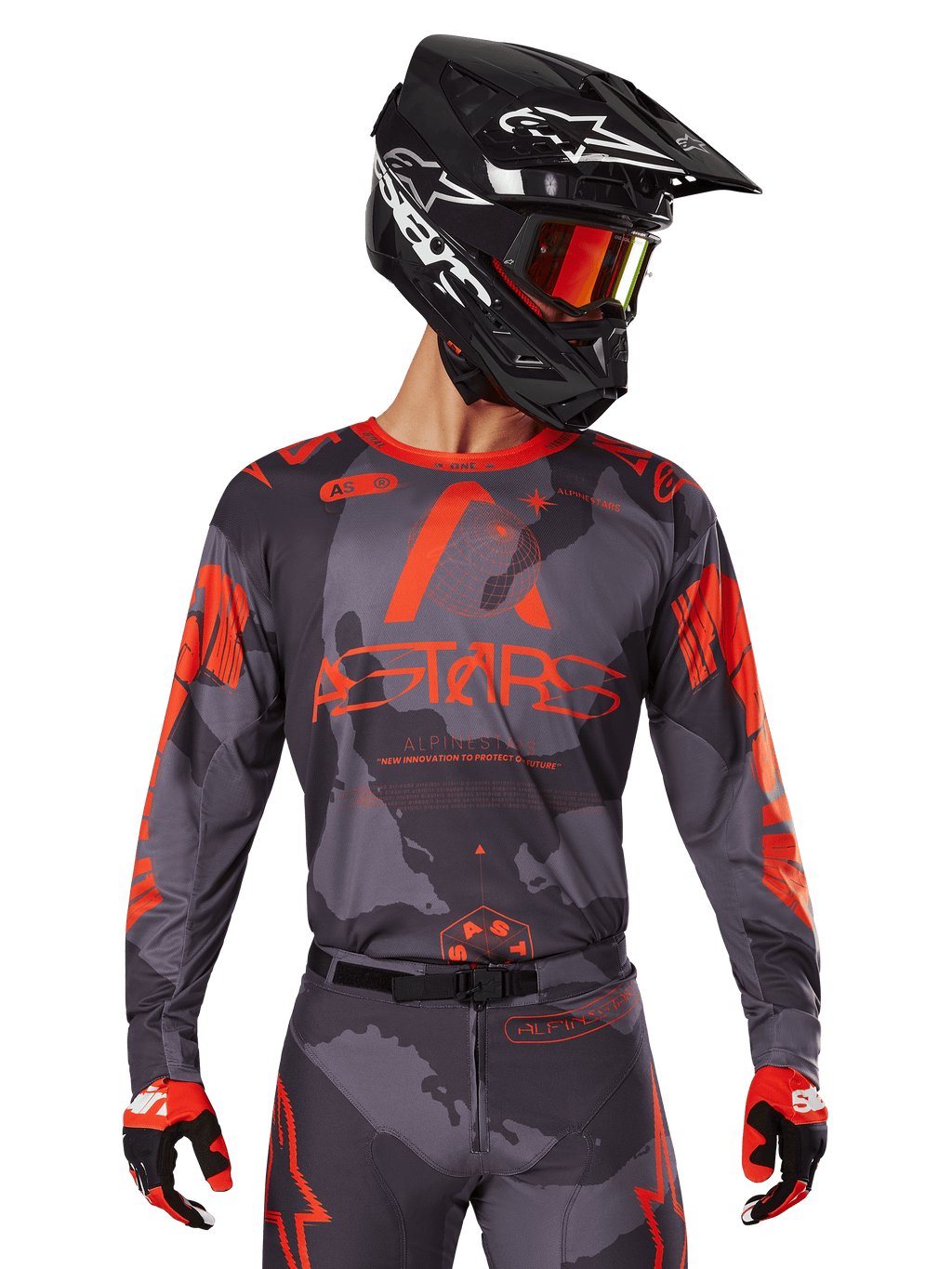 Alpinestars 2025 Racer Hollow Jersey, motorcross jersey, grijs camo en fluo oranje, gedragen met bijpassende kledingset inclusief broek en handschoenen, met een zwarte helm met witte graphics en crossbril, opvallende ASTARS-branding, beschermende off-road race-sportkleding