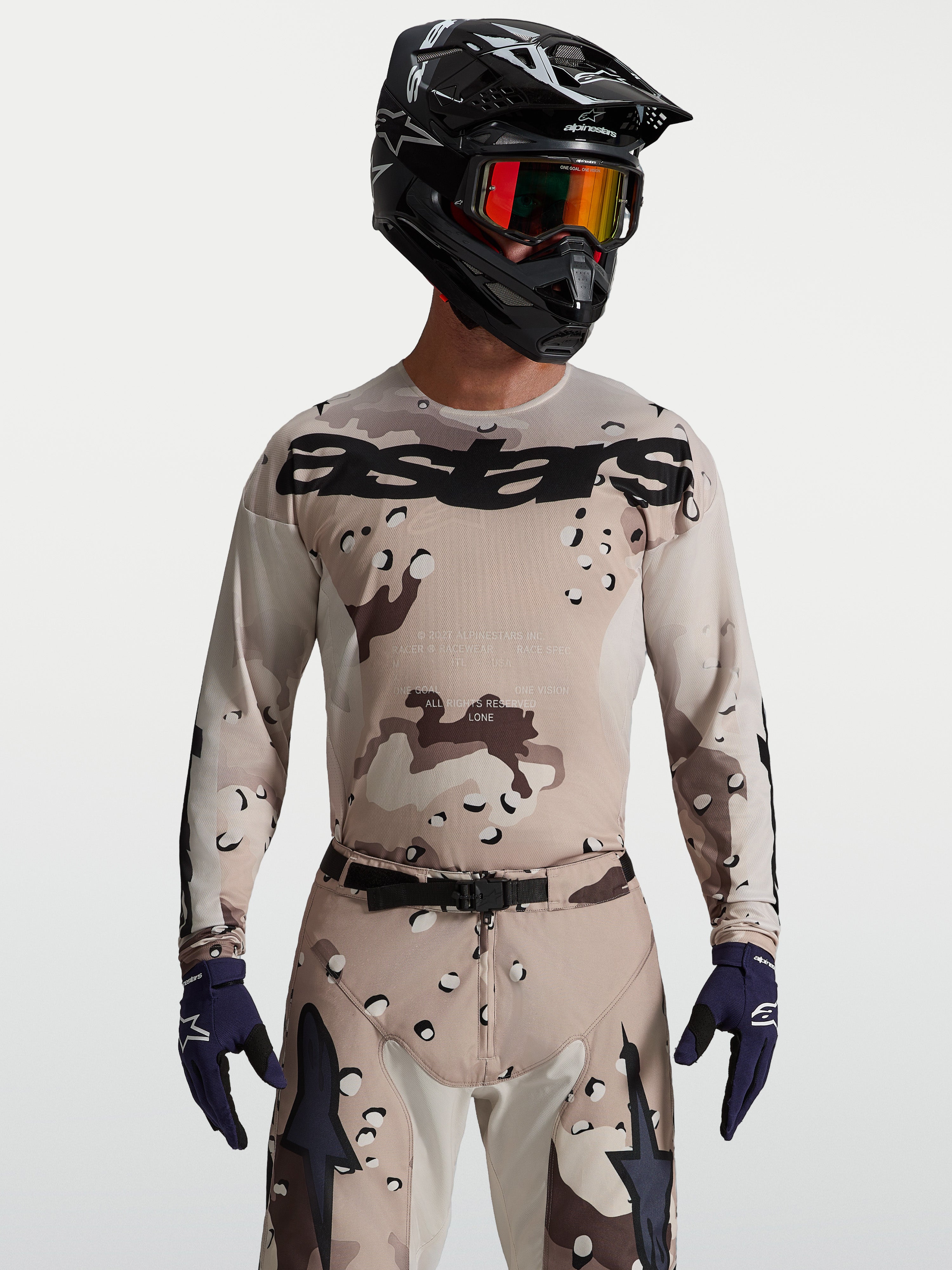 Alpinestars Racer Lone Jersey, heren-motocrossjersey in desert camo en zwart, op model met helm en veiligheidsbril.