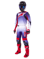 Motorcrosser in de Alpinestars 2025 Fluid Wurx Gear Set, paars en felrood jersey met witte accenten, bijpassende motorcrossbroek, felrode laarzen, zwarte helm met blauwe bril en rode en zwarte handschoenen, volledige professionele off-road race-uitrusting