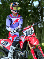 Motorcrosser op een rode Honda CRF crossmotor, draagt Alpinestars 2025 Fluid Wurx Jersey in paars en felrood, bijpassende paarse en rode broek, Red Bull-helm met gele crossbril, witte Alpinestars laarzen en handschoenen, professionele MX-uitrusting voor off-road rijden