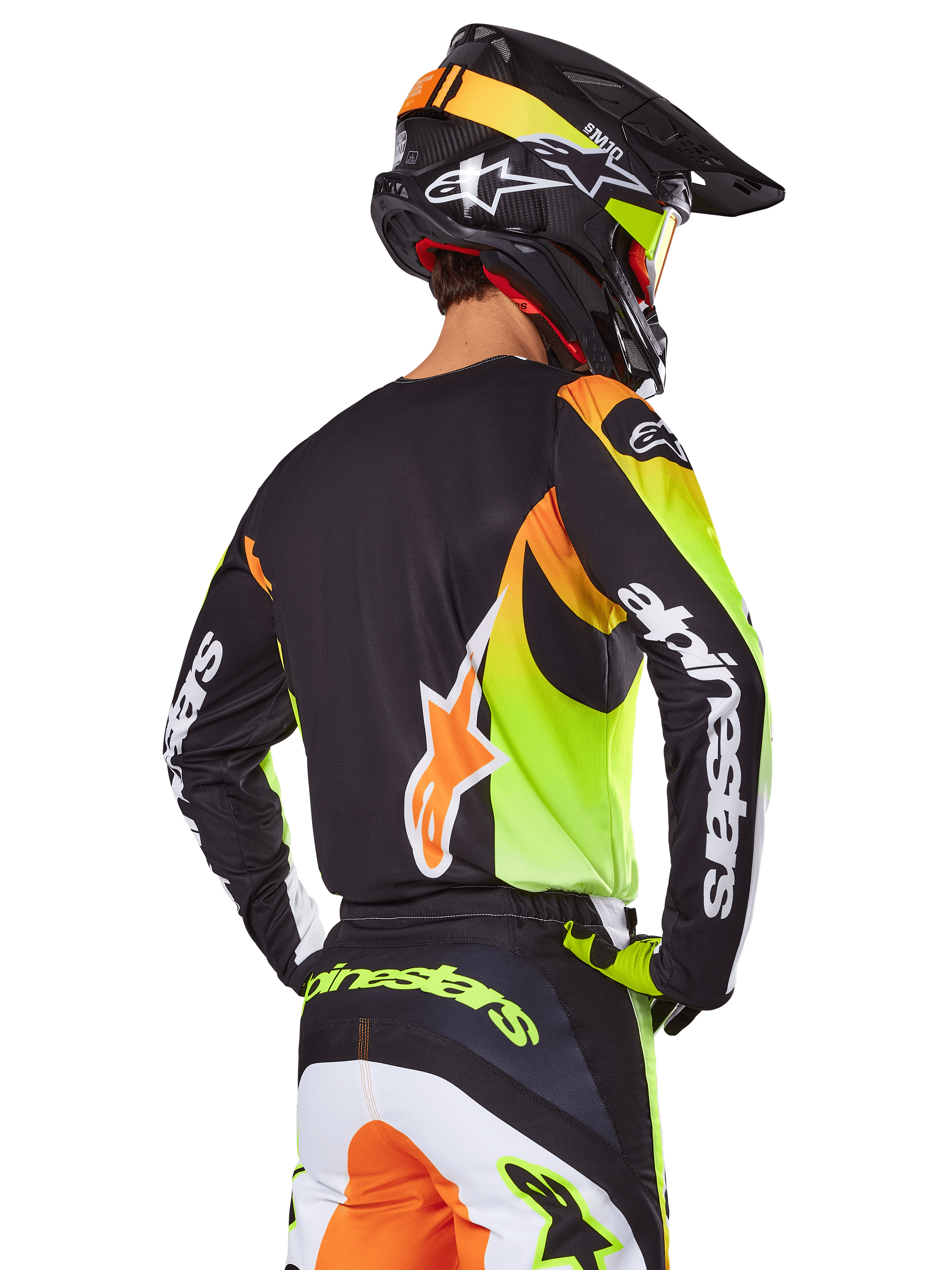 Motocross-Fahrer von hinten im Alpinestars 2025 Fluid Wurx Ausrüstungsset, schwarzes Trikot mit leuchtenden neongelben und orangefarbenen Grafiken, passende Hose mit weißen und orangefarbenen Einsätzen, schwarzer Helm mit Neon-Akzenten, markantes Alpinestars-Branding auf den Ärmeln und am Gesäß.