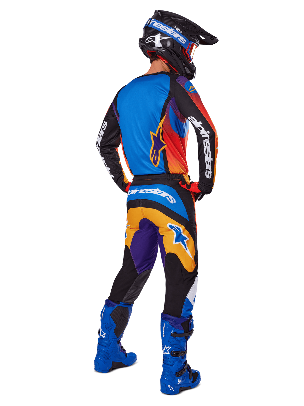 Pilote de motocross vu de dos portant l'ensemble d'équipement Alpinestars 2025 Fluid Wurx, maillot multicolore avec panneaux bleu, orange et violet, pantalon assorti avec logo Alpinestars blanc sur l'assise, bottes bleu vif et casque noir, tenue coordonnée pour la course tout-terrain