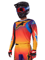 Set d'équipement Alpinestars 2025 Fluid Wurx, ensemble de motocross, dégradé orange, violet et bleu, avec un grand logo A-stars noir, porté avec un casque noir et des lunettes bleues, tenue coordonnée pour la course tout-terrain professionnelle