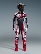 Motocross rider wearing full Alpinestars racing gear, 2026 Techstar Nomur Jersey in Black White Red, matching pants with red accents, black helmet, and bright red boots, features large red Astars logo on chest with speckled gradient pattern, coordinated outfit for off-road competition